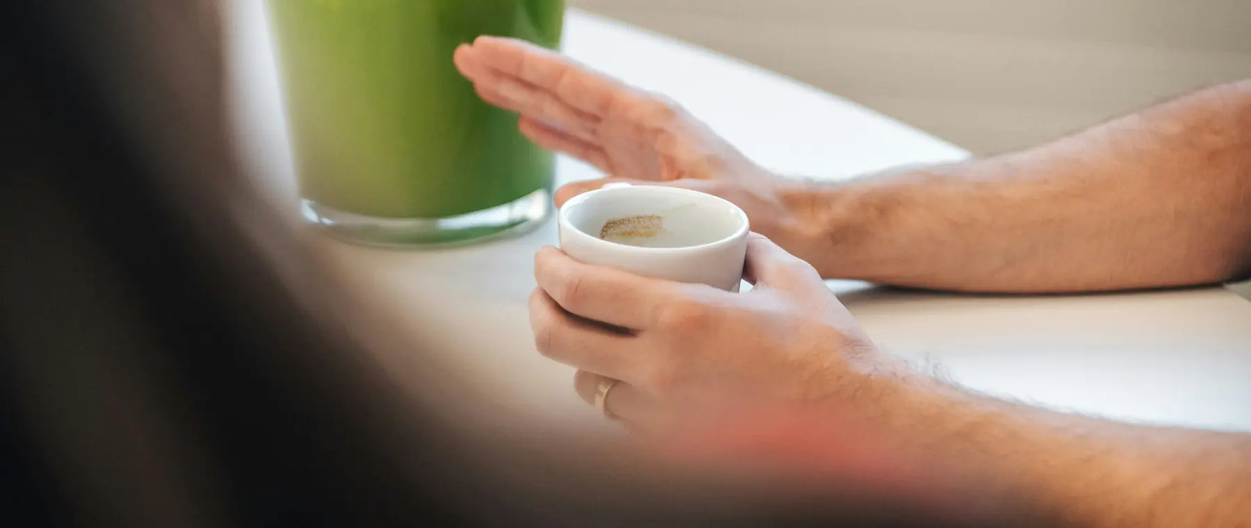 Hands holding a cup of tea beside a green plant