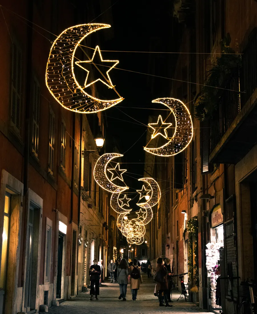Crescent moon and star lanterns glowing above a quiet evening street