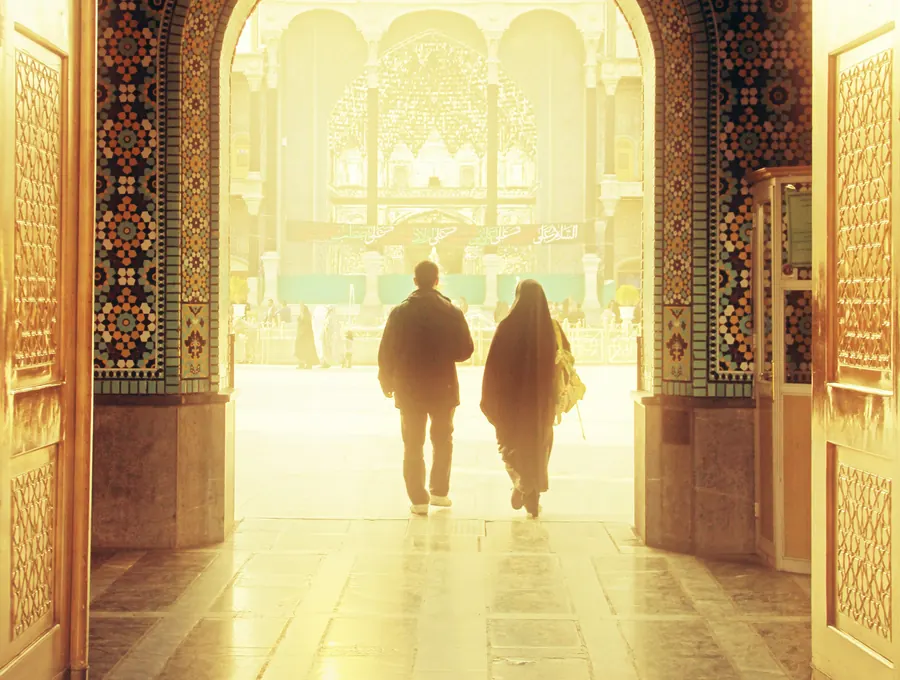 Two people walking through a sunlit mosque archway