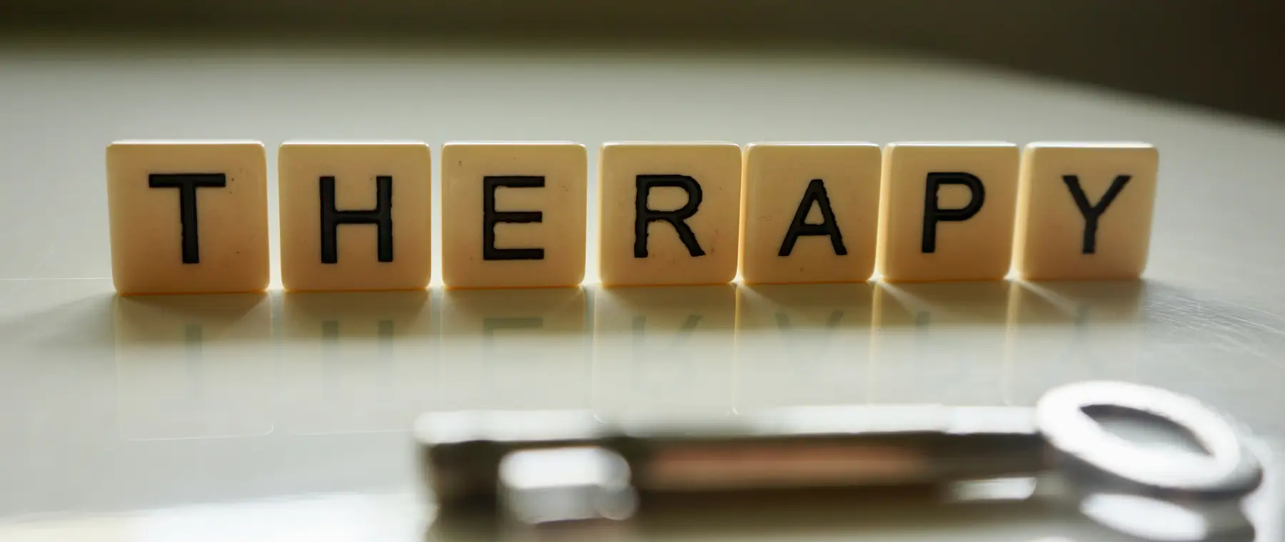 Wooden letter tiles spelling the word therapy beside a key