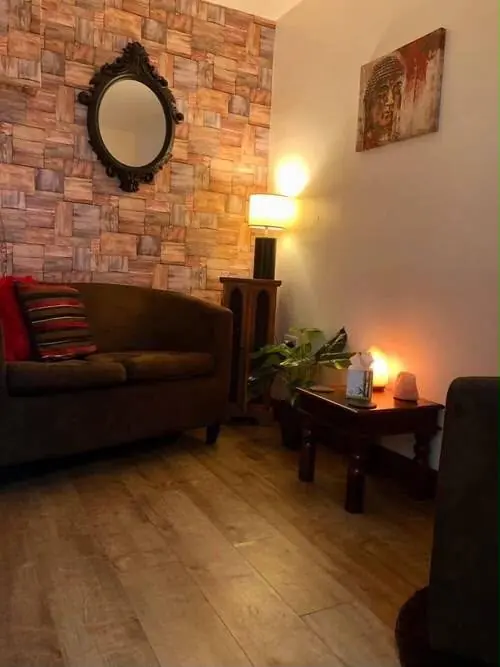 A cosy therapy room with a brick feature wall, a brown sofa and a warm lamp