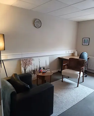 A calm room with a black leather armchair, a wooden desk and a soft lamp
