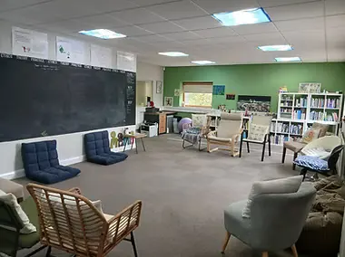 A large, bright room with a chalkboard, bookshelves and a mix of comfortable chairs