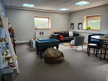 A spacious room with a sofa, a round table and a bean bag, lit by two windows