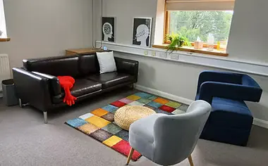 A room with a black leather sofa, grey and blue armchairs and a colourful rug