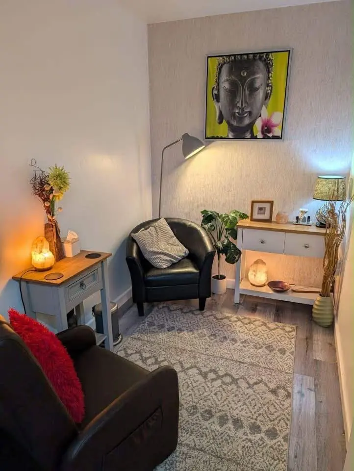 A softly lit room with candles, a side table, an armchair and a bright portrait on the wall